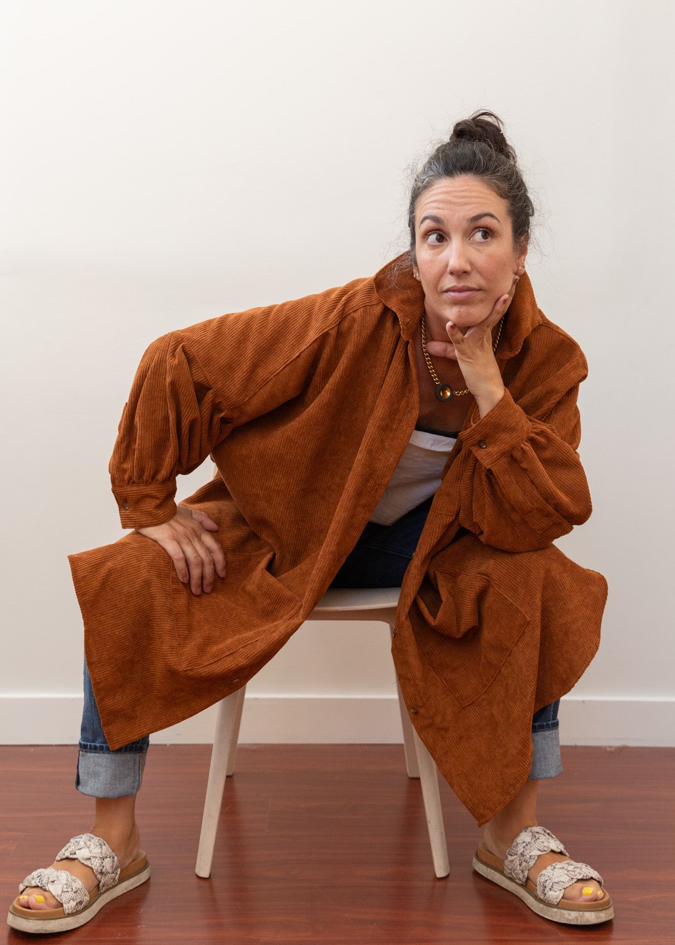 Woman sitting on a chair leaning forward on knees with a corduroy jacket drooping over