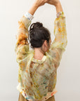 The back of a model wearing a see-through silk top with notes of yellow, green and orange in a tie-dye type style.