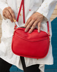 A woman holding a vivid red, cherry-colored cube-shaped bag, putting a zerra & co lipgloss into the crossbody, shoulder bag