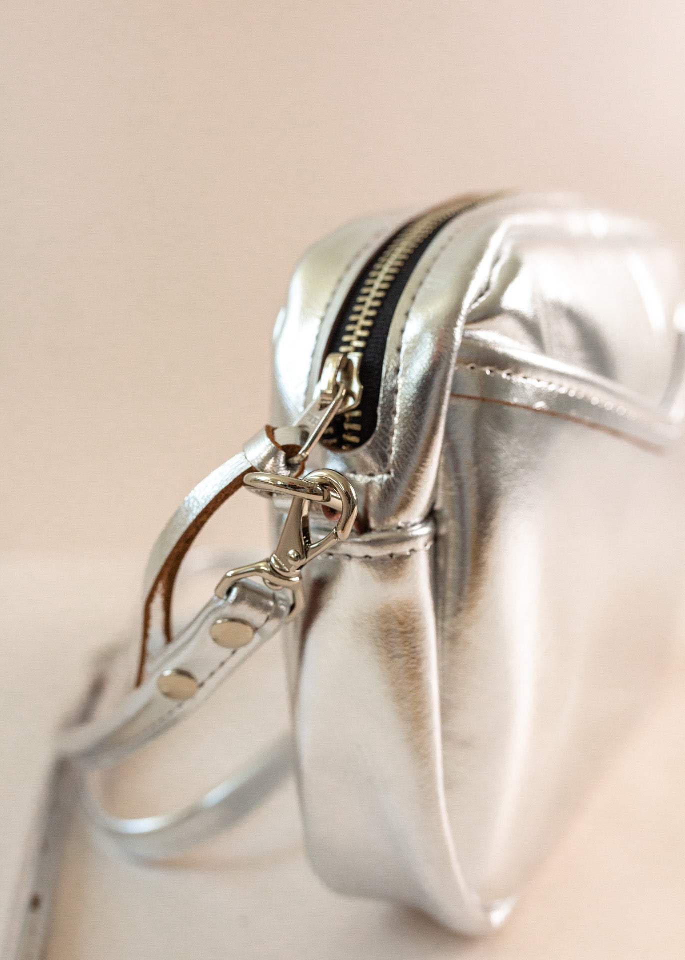 Close-up of cubist handbag in silver, with a v-shaped front pocket and a long thin shoulder strap