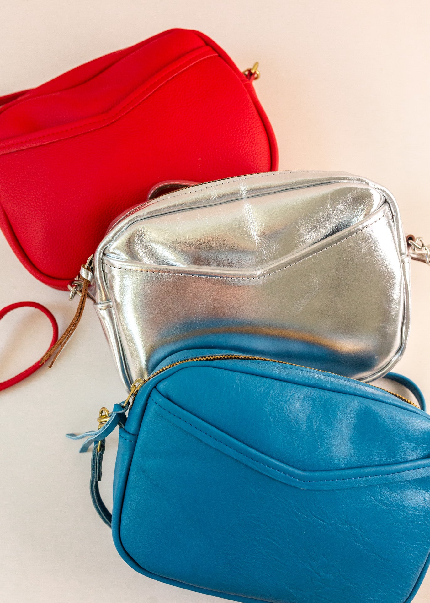 Layer of cubist handbags, with a v-shaped front pocket and a long thin shoulder strap, in cherry, silver and azure