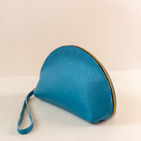 Azure, or blue, colored shell bag standing up on a light pink background with a short wrist handle
