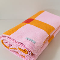 Folded up pink, orange and red blanket on a white background