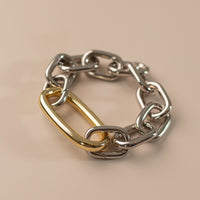 Photo of an oval link bracelet in silver with a large oval link in gold on a peach background