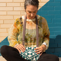 a woman sitting in front of a brick wall with an aztec designed crossbody bag around her neck