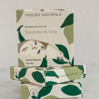 Two boxes of shower steamers with one standing up on top. Boxes are white and green and "spearmint and lime" scented