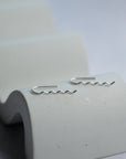 Silver wavy earrings on a textured white stand with a light gray background