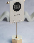 Silver hoop earrings on a stand with 'Baleen' brand label on a gray background