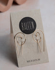 Gold earrings on a 'BALEEN' branded card with a wavy object in the background