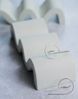 Silver sculpted hoops on a wavy stand against a light gray background