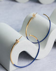 Gold and cobalt blue hoop earrings on a white stand