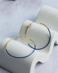 Gold and blue hoop earrings on a white stand with a light gray background