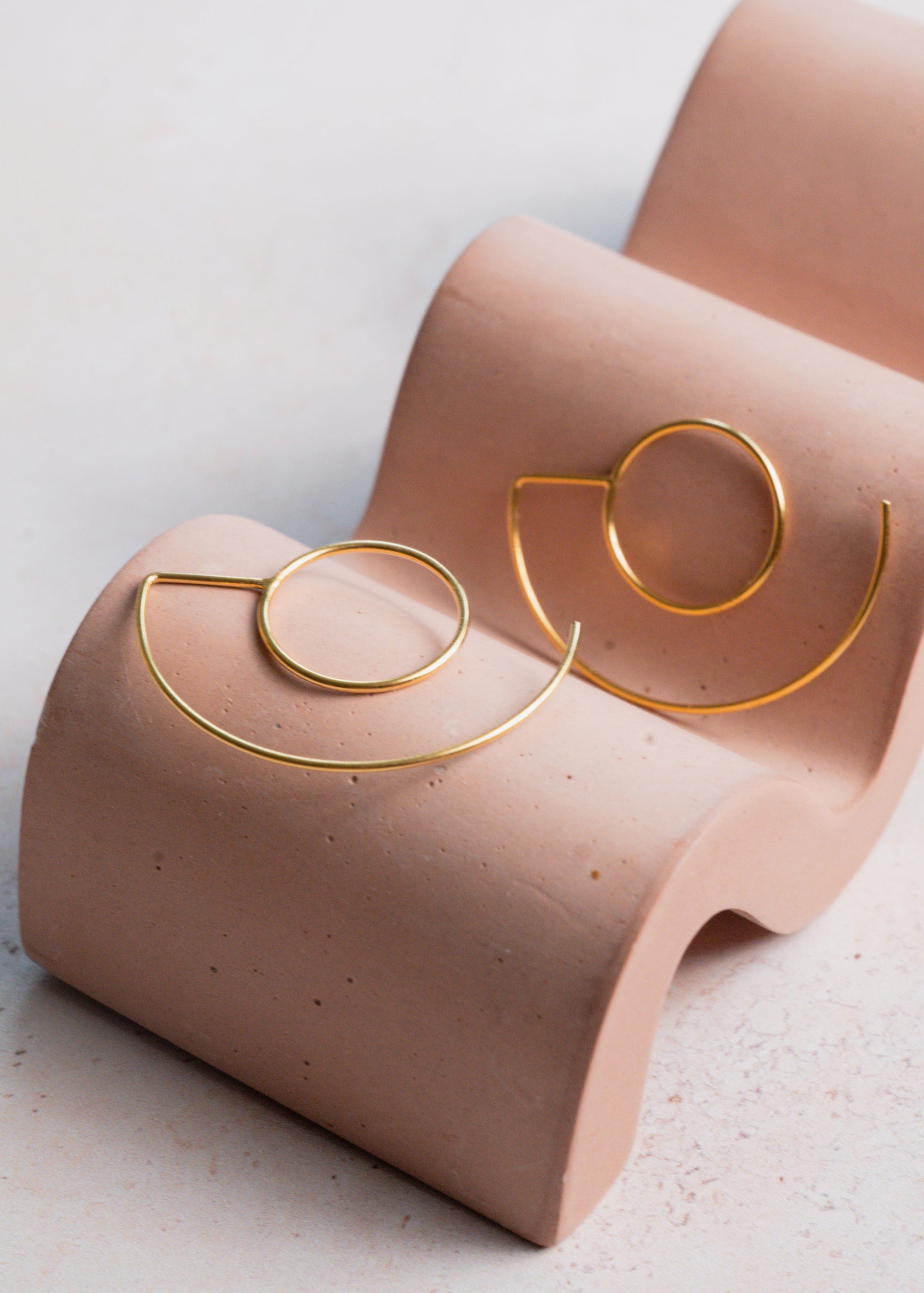 Gold hoop earrings on a pink display stand against a light background