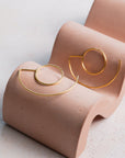 Gold hoop earrings on a pink display stand against a light background