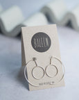 Baleen silver hoop earrings on a branded card with a gray background