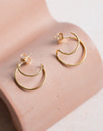 Gold hoop earrings on a pink concrete display against a neutral background