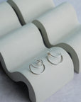 Silver hoop earrings on a concrete jewelry display against a light gray background
