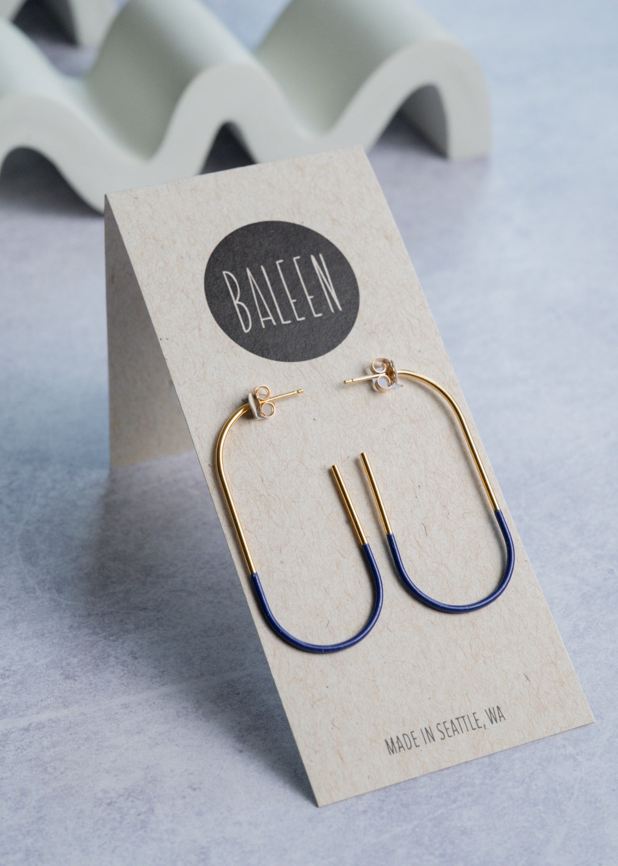 Gold and blue hoop earrings on a Baleen branded card with a light gray background