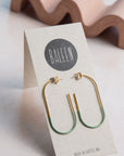Gold and green earrings on a 'BALEEN' branded card with a wavy object in the background.