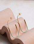 Gold and mint hoop earrings on a wavy pink stand with a neutral background