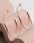 Gold and green hoop earrings on a wavy pink surface