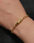 A gold bar block bracelet worn on a person's wrist, showcasing a chain link design with a bar charm.