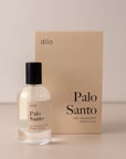 Bottle of perfume by dilo, with a cream label on the front stating “palo Santo. eau de parfum, 50 ml. made in the usa" with the cream box that it comes in in the background