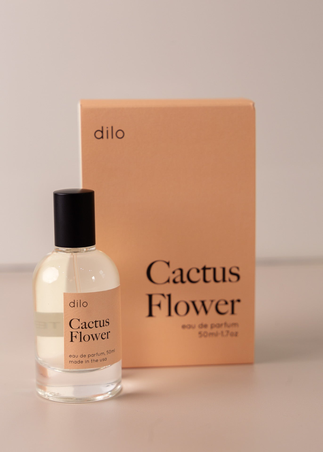 Bottle of perfume by dilo, with a pink label on the front stating “cactus flower. eau de parfum, 50 ml. made in the usa" with the pink box that it comes in in the background