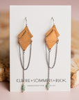 Pair of gold and silver Morning Star earrings by Claire Sommers Buck shown on white card with a pink background