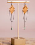 Pair of gold and silver Morning Star earrings by Claire Sommers Buck shown on stand with a pink background