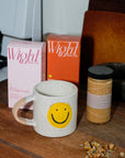 Smiley face mug with Wight Tea Co. tea boxes and a jar of Hon's Honey on a kitchen counter.