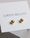 Gold woven ball earrings by Gwen Beloti displayed on a concrete block.