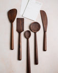 Set of walnut wooden kitchen utensils including spatulas and spoons on a light background