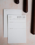 Recipe card front and back shown on a light surface with dark cylindrical objects