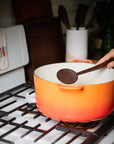 Walnut hand carved wooden spoon shown in use with a vintage orange Le Crueset cast iron pot