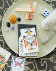 Colorful oracle cards, prayer candle, palo santo, sage and matches on a dish.