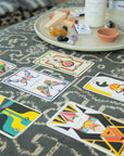 Colorful geometric oracle cards spread on a textured surface with a tray of crystals, sage, and palo santo.