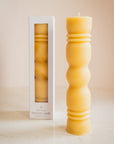 Beeswax candle with textured design next to its packaging on a beige background