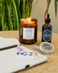 Collection of items including a notebook, candle, tincture, salve and matches on a table.