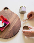 Wooden cutting board with colorful napkins, jar of salt and a small ceramic bowl and spoon on a table.