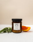 photo of a candle labeled "lucid dream" with orange halves and sage besides the candle on a white and light pink background