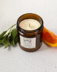close up of a candle labeled "lucid dream" with orange slices and sage besides the candle on a white background