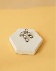 A pair of pearl and silver earrings displayed on a white hexagonal platform with a yellow background.