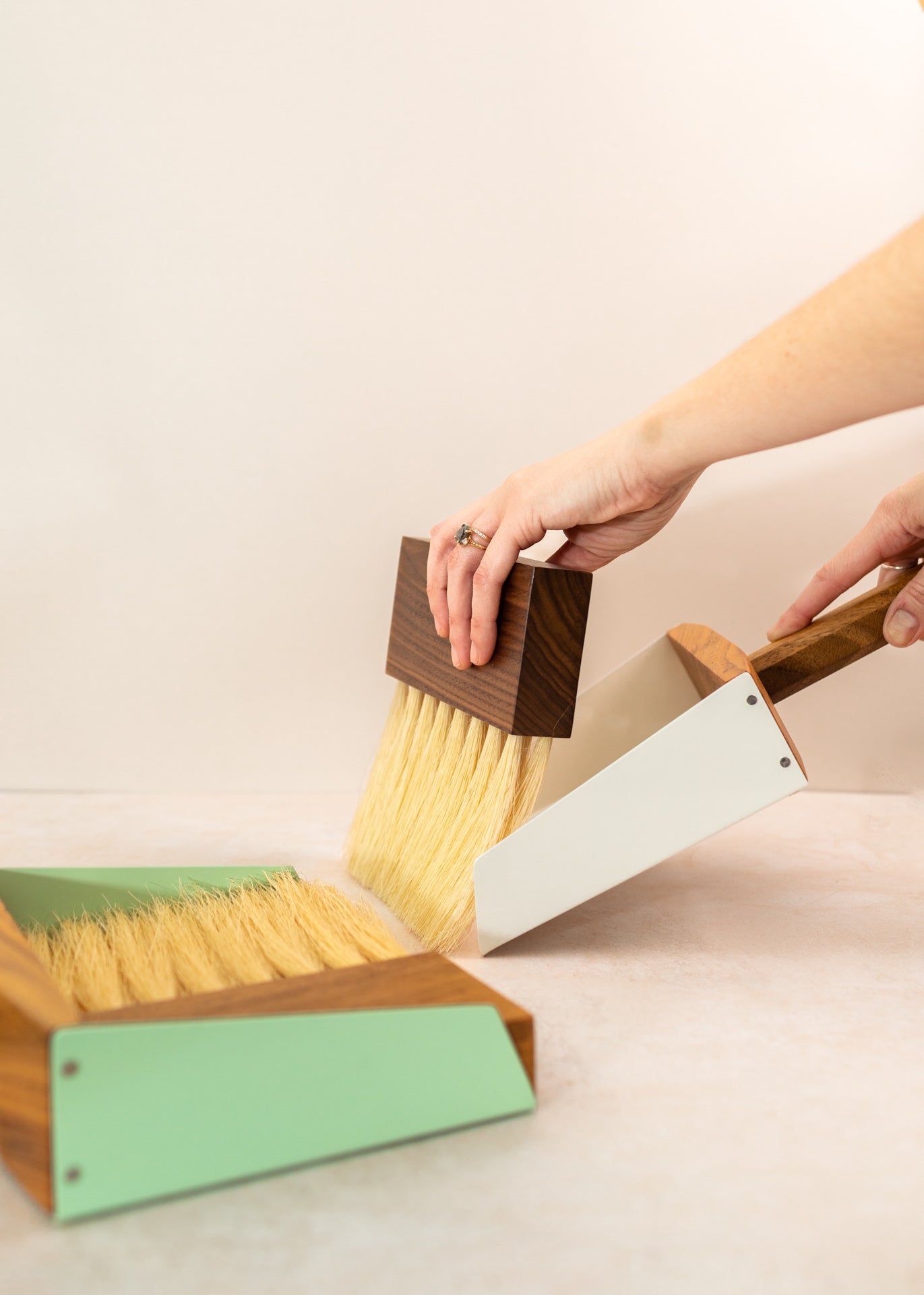 two mini dust pan sets with arms sweeping with the white set while the green is in the foreground