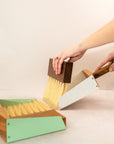 two mini dust pan sets with arms sweeping with the white set while the green is in the foreground