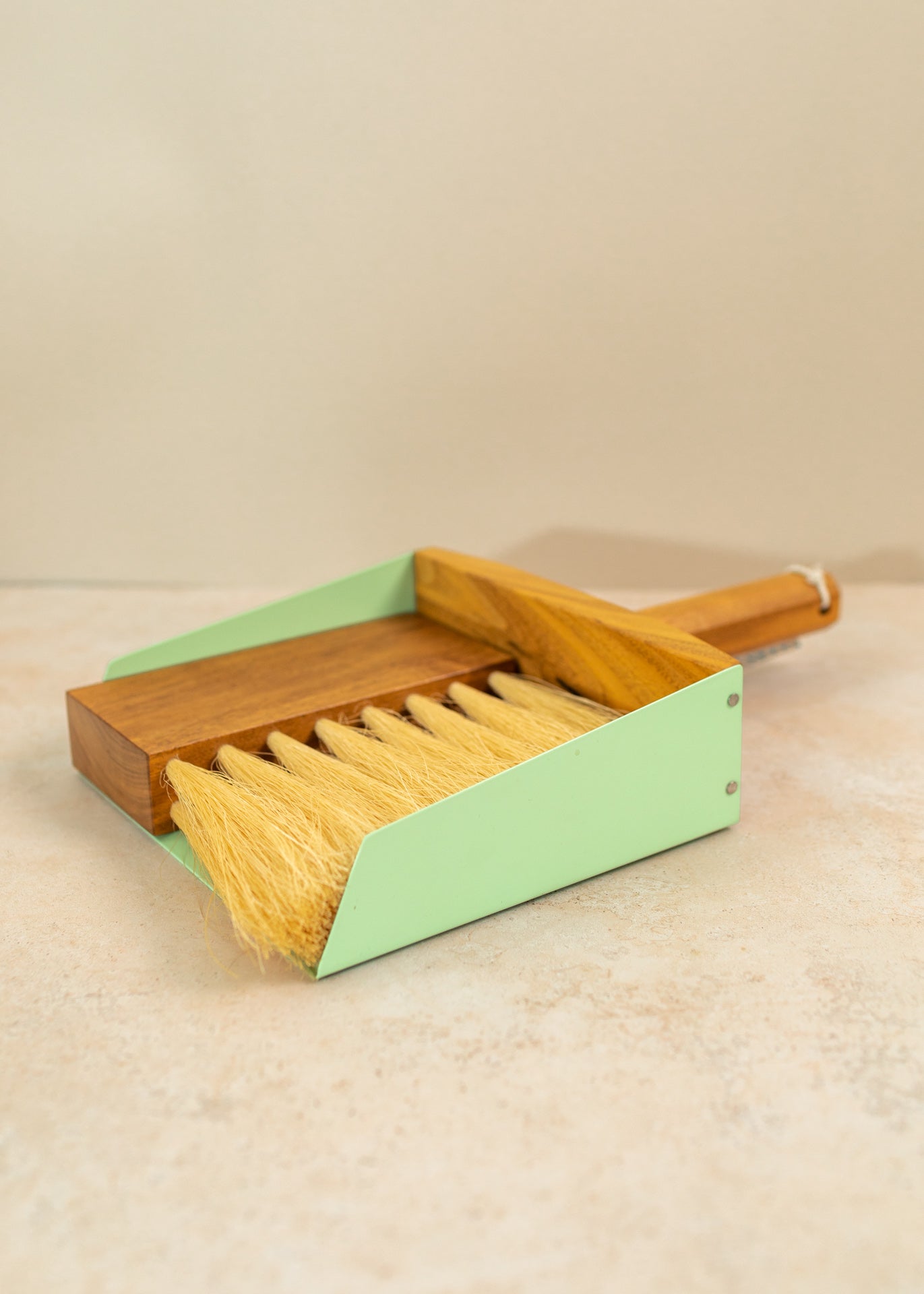 a mint green mini dust pan set on a pink background