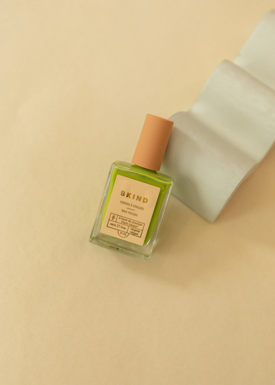 Flatlay of a nail polish bottle leaning on a white ceramic. Color of nail polish is lime green called "mojito"