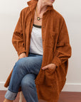 Front view of model wearing a rust colored shacket sitting down and un bottoned