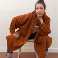 Woman sitting on a chair leaning forward on knees with a corduroy jacket drooping over