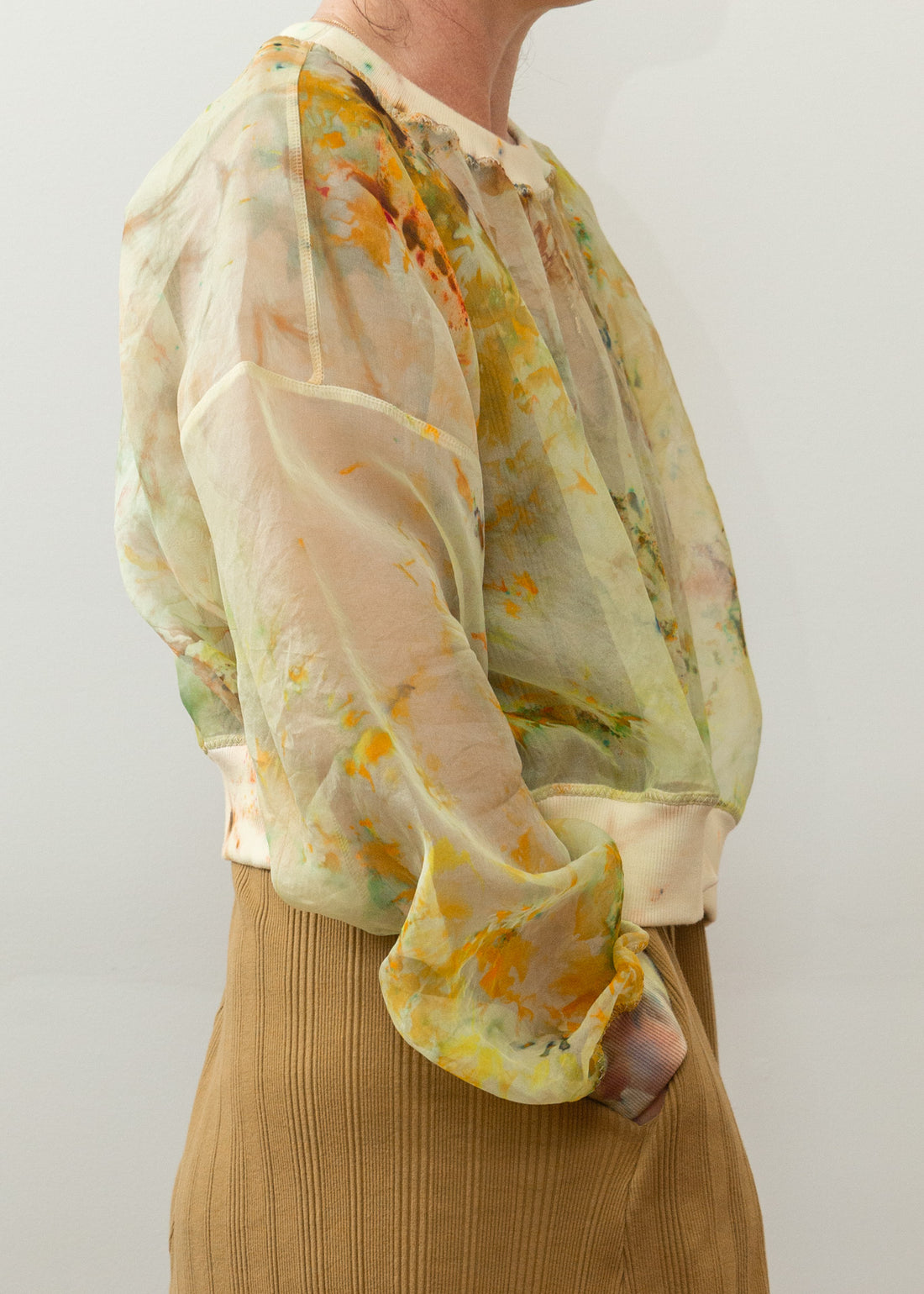 The side of a model wearing a see-through silk top with notes of yellow, green and orange in a tie-dye type style.